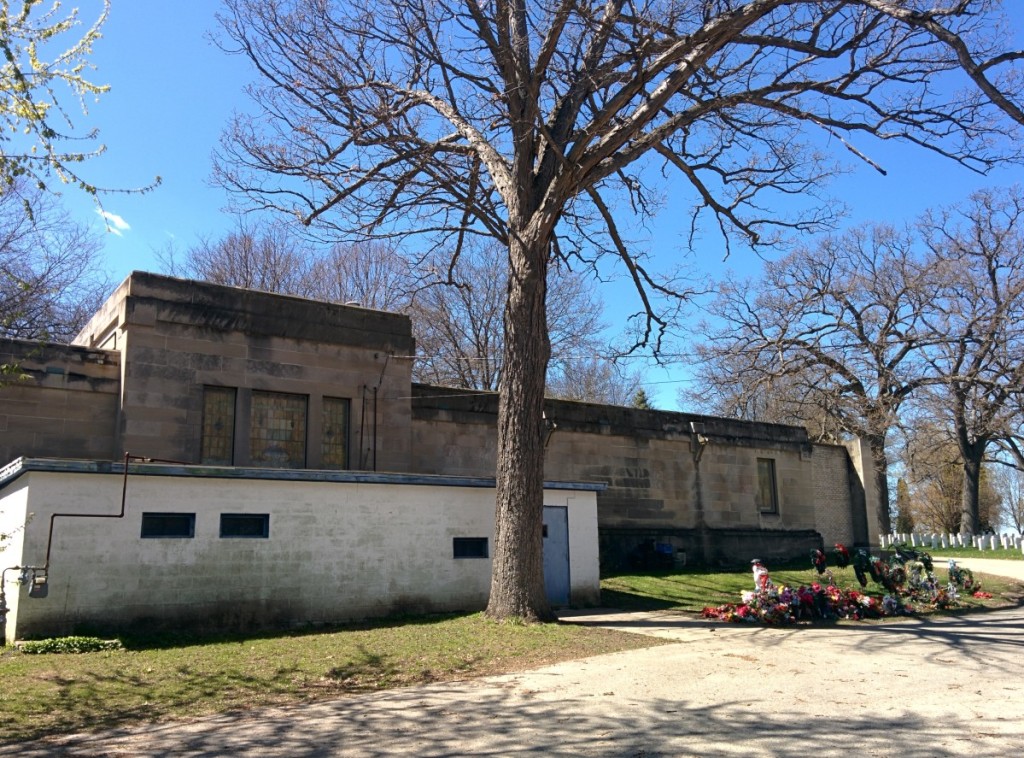 The white crematory building still stands behind the mausoleum. Decorations removed from the graves after the winter stand collected to one side. Photo by Kevin Walters.
